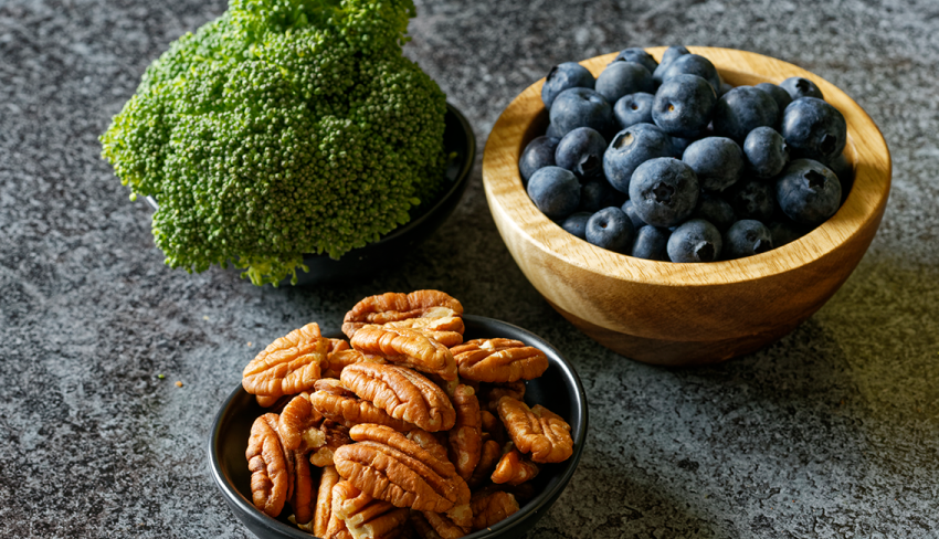 Close up of bowls of broccoli, blueberries, and pecans resting on a counter. All three foods are great for bladder health!