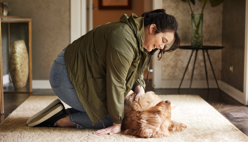 A woman plays with her dog on a rug in her living room. The right absorbency product can give her peace of mind to have fun.