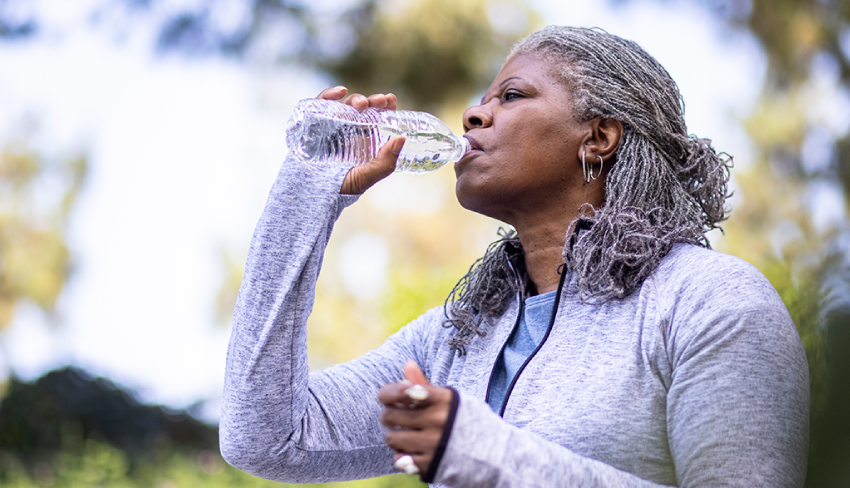 A woman in workout gear drinks from a water bottle. Hydration is vital to bladder health as well as odor control.
