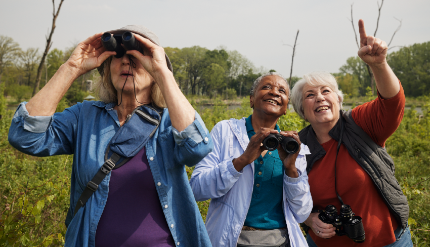 Three women birdwatching in a field. When dealing with UI, it's important to keep doing what you love to keep your spirits up.
