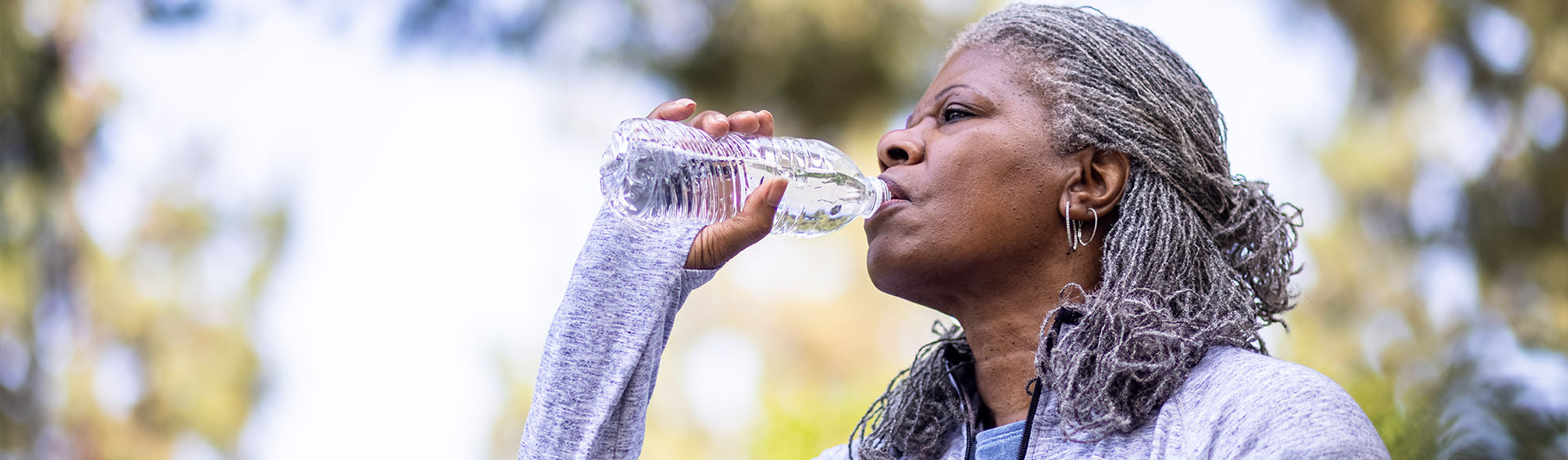 A woman in workout gear drinks from a water bottle. Hydration is vital to bladder health as well as odor control.