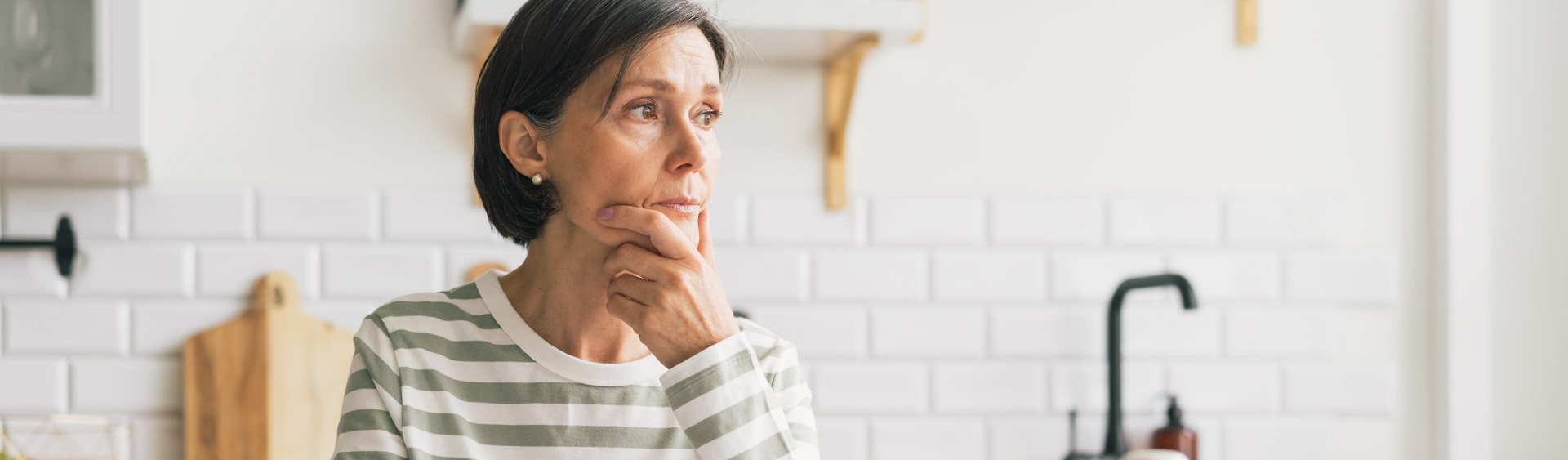A woman sits, resting her chin on her hand, looking worried. Her anxiety can exacerbate her incontinence.