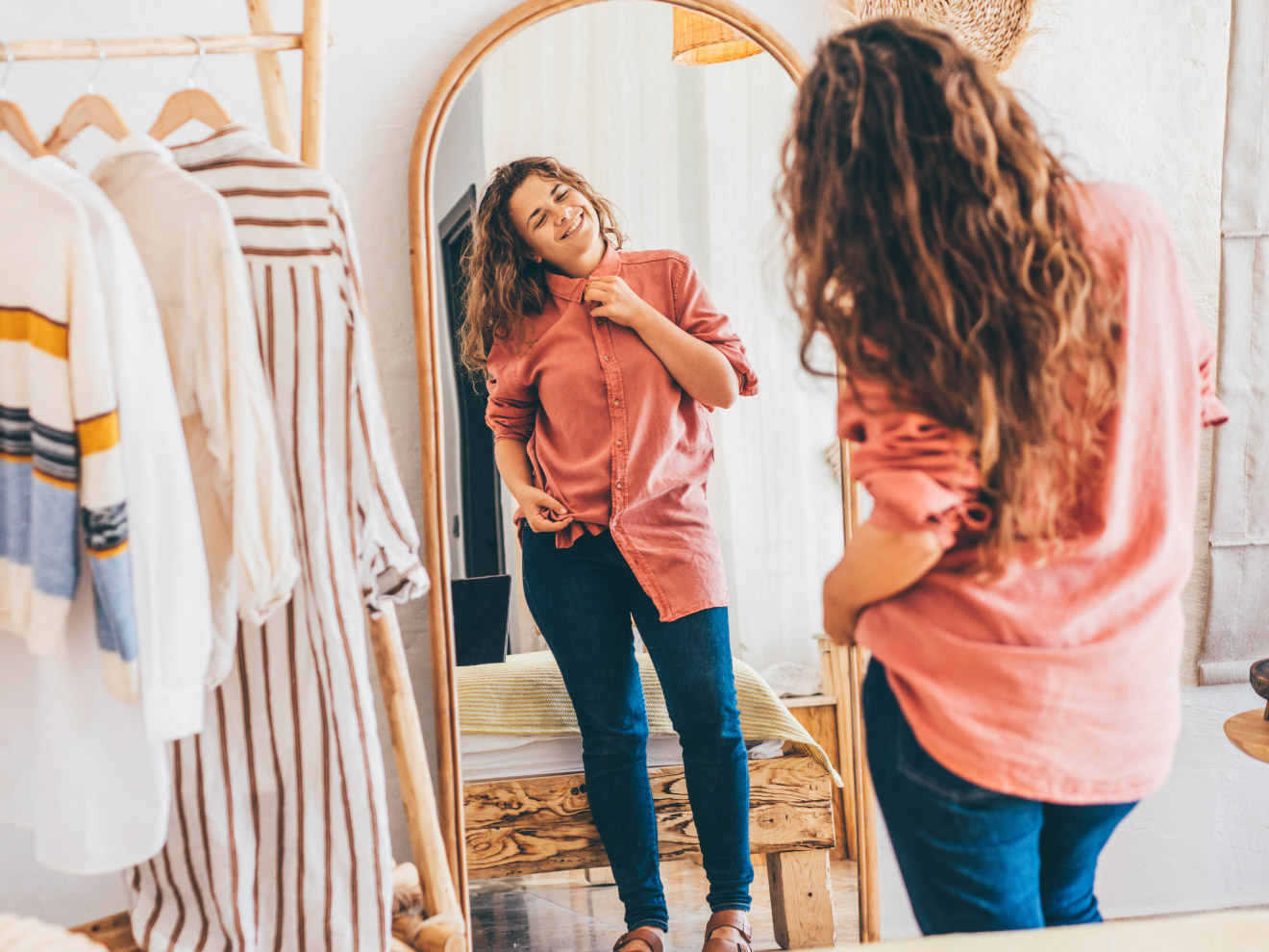 A woman examines her outfit in the mirror: a flowy shirt with dark wash jeans, fashionable but functional for handling leaks.