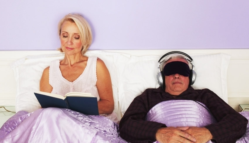 A woman reads in bed beside her sleeping partner. Her smart bedtime routine ensures a restful night without pee breaks.