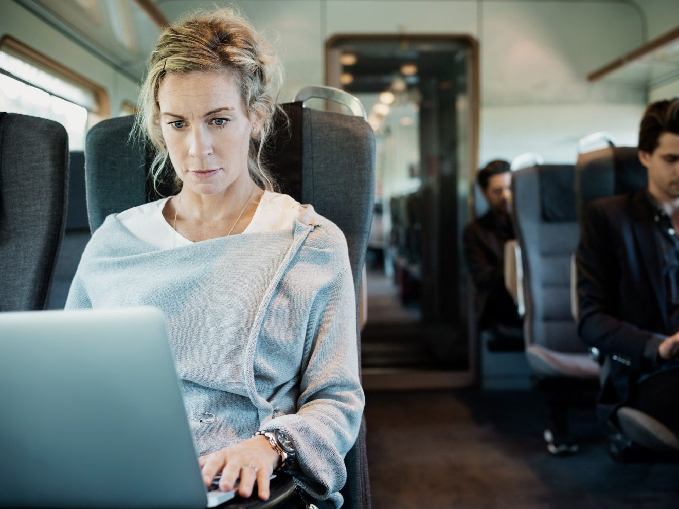 A woman works on her laptop on a plane, able to fully focus without leak anxiety thanks to her travel prep. 